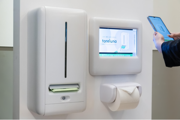 トイレ個室内に設置されたトレルナ端末とデジタルサイネージの利用イメージ