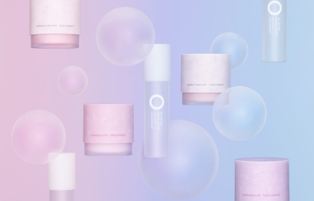 「hada to kokoro(肌と心)」のオールインワンクリーム化粧水(90ml)の商品単体写真。左にはマットなすりガラス調の白いポンプボトル、右には「オールインワン クリーム化粧水/化粧水・乳液・美容液・クリーム」と記載されたブルーからピンクへのグラデーションが美しいホログラフィック調の外箱が並んでいる。白背景でシンプルに撮影されている。
